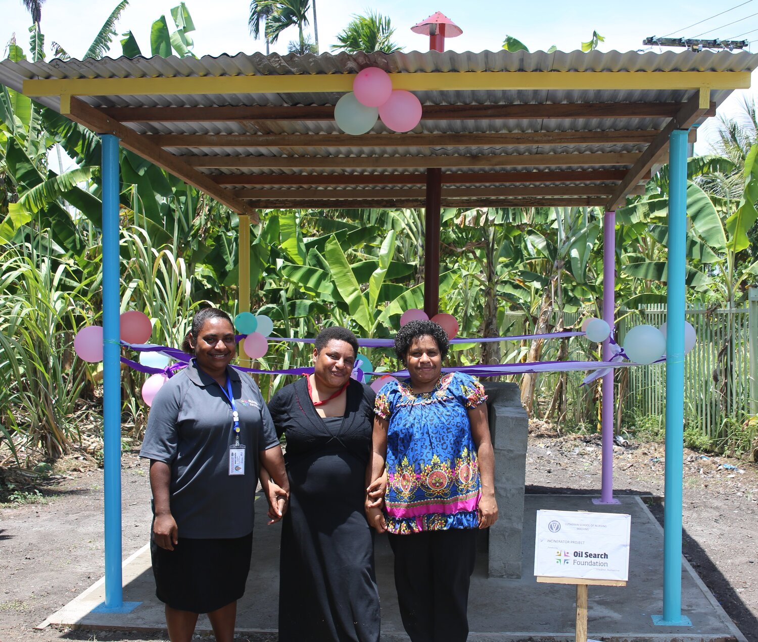 Three PNG women standing holding hands and smiling.