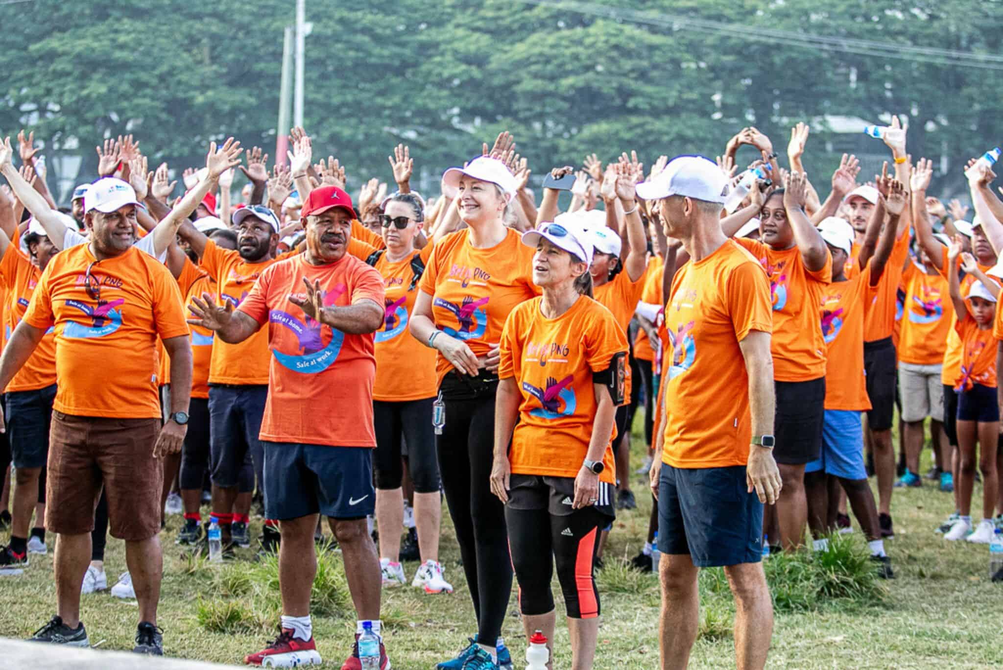 Group of people in orange shirts with hands over their heads